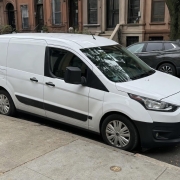 A parked vehicle along a Brooklyn rowhouse block with brownstone stoops and curbside parking