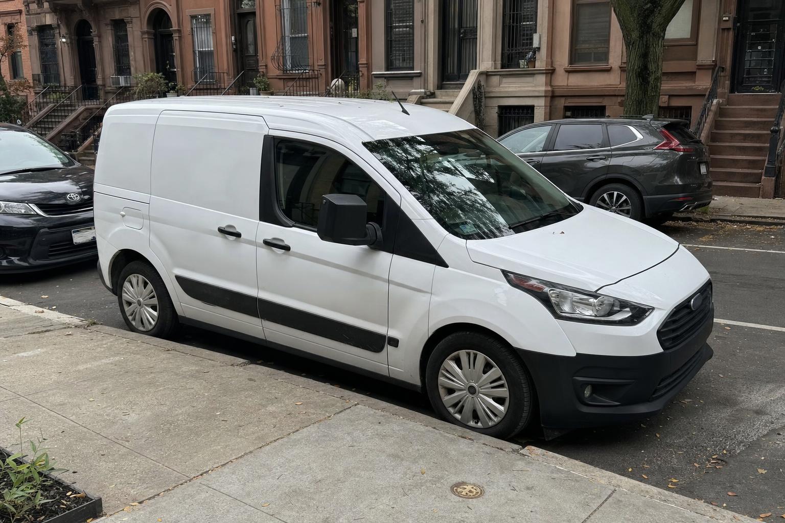 A parked vehicle along a Brooklyn rowhouse block with brownstone stoops and curbside parking
