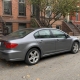 A car parked beside brownstone rowhouses on a Brooklyn residential street.