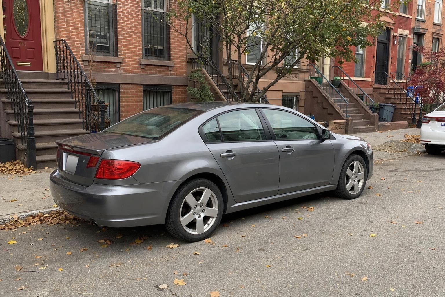 A car parked beside brownstone rowhouses on a Brooklyn residential street.