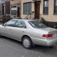Silver sedan parked beside brownstone stoops on a Brooklyn residential street in autumn.