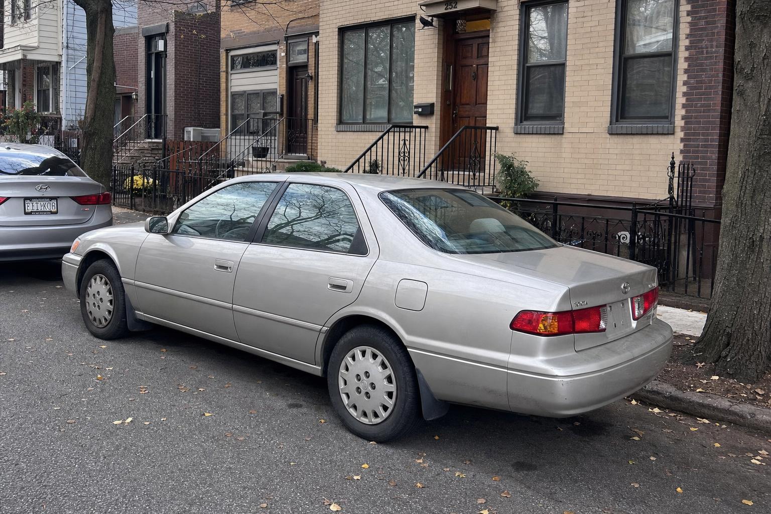 Silver sedan parked beside brownstone stoops on a Brooklyn residential street in autumn.