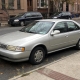 Silver sedan parked beside Brooklyn brownstones with stoops and autumn leaves along the curb.