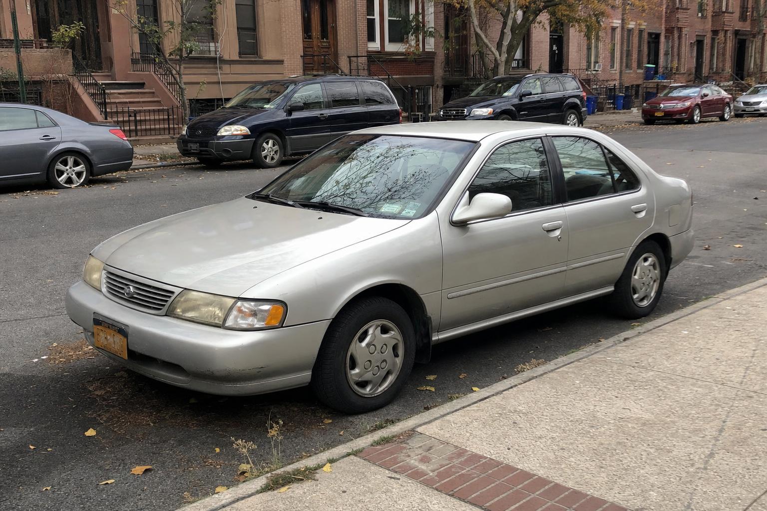 Silver sedan parked beside Brooklyn brownstones with stoops and autumn leaves along the curb.