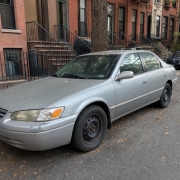 Vehicle Parked on a Brooklyn Rowhouse Block Silver sedan parked beside a Brooklyn sidewalk with brick rowhouses and brownstone stoops.