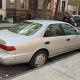 Silver sedan parked beside brownstone stoops on a Brooklyn residential street.