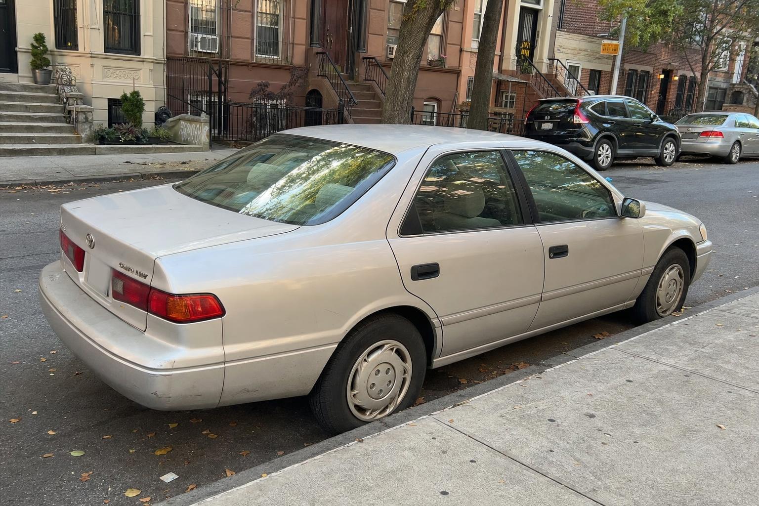Silver sedan parked beside brownstone stoops on a Brooklyn residential street.