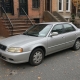 Silver sedan parked along a Brooklyn brownstone block with stoops and autumn leaves.