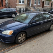 Parked Sedan on a Brooklyn Brownstone Block Dark blue sedan parked beside brownstone stoops on a Brooklyn residential street.