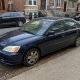 Dark blue sedan parked beside brownstone stoops on a Brooklyn residential street.