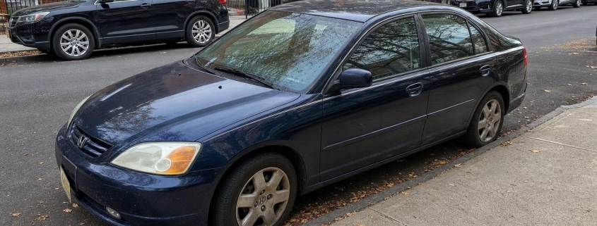 Dark blue sedan parked beside brownstone stoops on a Brooklyn residential street.