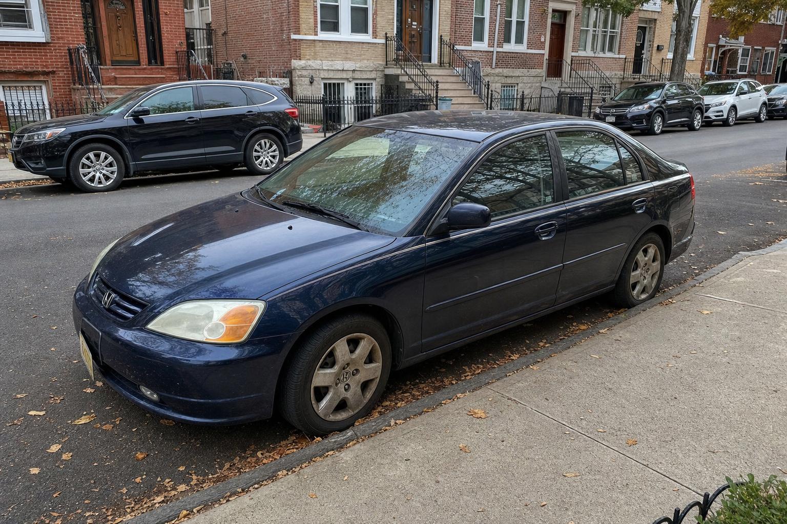 Dark blue sedan parked beside brownstone stoops on a Brooklyn residential street.