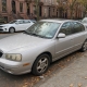 An older passenger car parked curbside beside Brooklyn brownstones with raised stoops.