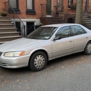 Brooklyn Vehicle Donation, Trade-In or Sale Silver sedan parked beside brick rowhouses and stoops on a Brooklyn residential street.