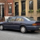 An ordinary used car parked along a Brooklyn brownstone block with stoops and curbside parking.