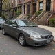 Used sedan parked beside brownstone stoops on a Brooklyn residential street in autumn.
