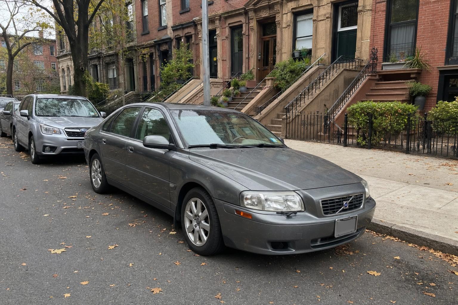 Used sedan parked beside brownstone stoops on a Brooklyn residential street in autumn.