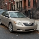 Older sedan parked beside brick rowhouses and brownstone stoops on a Brooklyn street in autumn.
