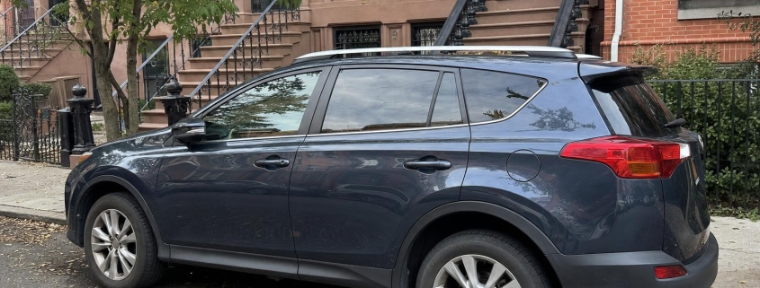Unbranded vehicle parked beside brownstone stoops on a Brooklyn residential street