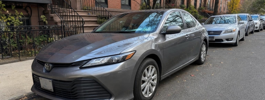 A parked sedan on a Brooklyn residential street with brownstone buildings nearby