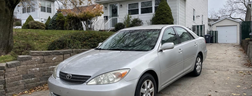 Silver sedan parked in a Staten Island driveway beside detached homes and mature trees.