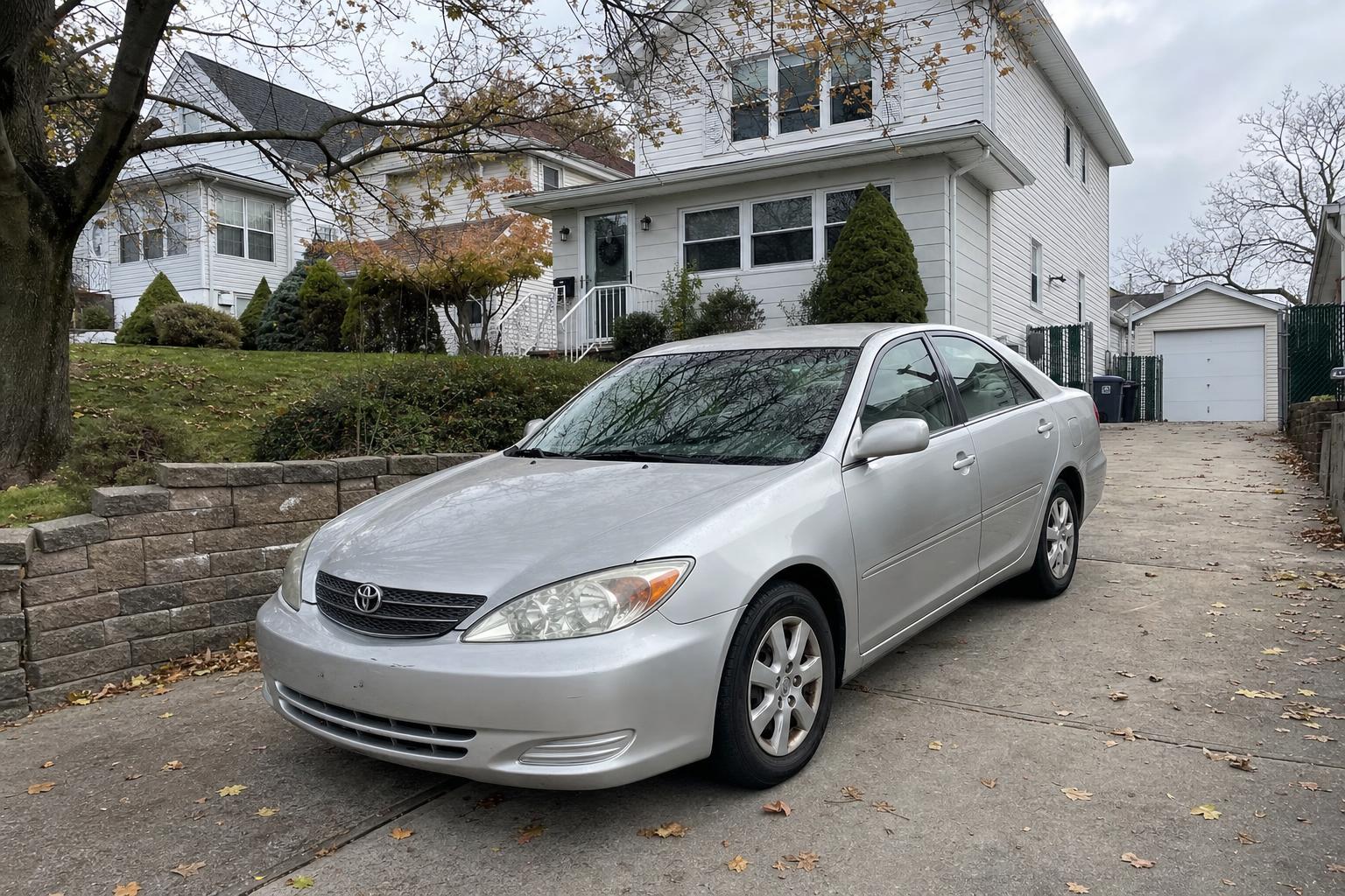 Silver sedan parked in a Staten Island driveway beside detached homes and mature trees.