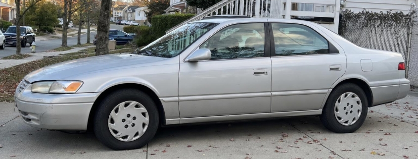 Silver sedan parked in a Staten Island driveway beside detached homes and autumn trees.