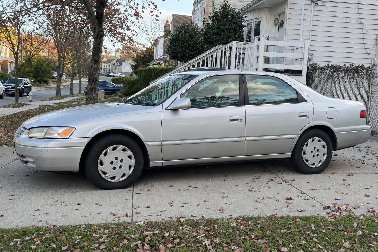 Silver sedan parked in a Staten Island driveway beside detached homes and autumn trees.