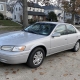 Older silver sedan in a Staten Island driveway beside detached homes and autumn trees.