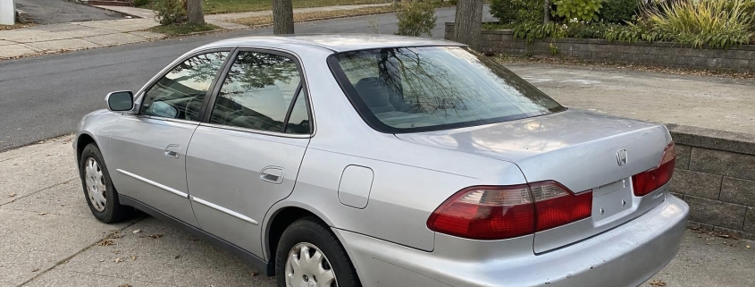 Silver sedan in a Staten Island driveway beside detached homes and autumn trees.