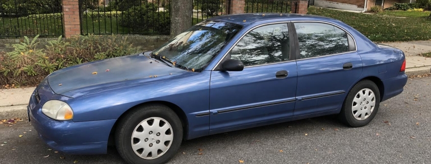 A blue sedan parked on a tree-lined Staten Island residential street