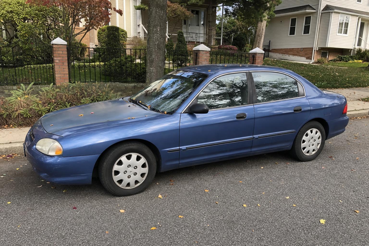 A blue sedan parked on a tree-lined Staten Island residential street
