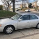 Older silver sedan in a Staten Island driveway beside detached homes and autumn trees