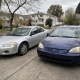 Two used cars parked side by side in a Staten Island residential driveway near detached homes.