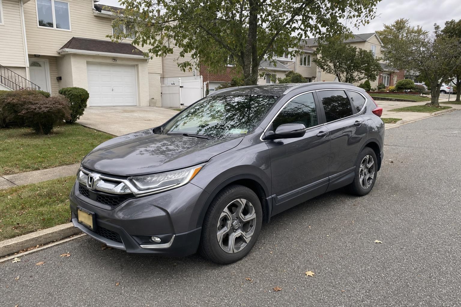 A gray Honda CR-V parked on a Staten Island residential street in front of detached homes and trees.