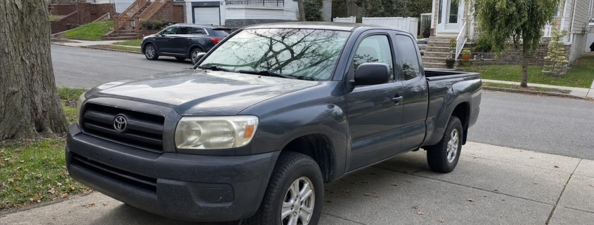 Used pickup truck parked in a Staten Island driveway beside detached homes and mature trees.