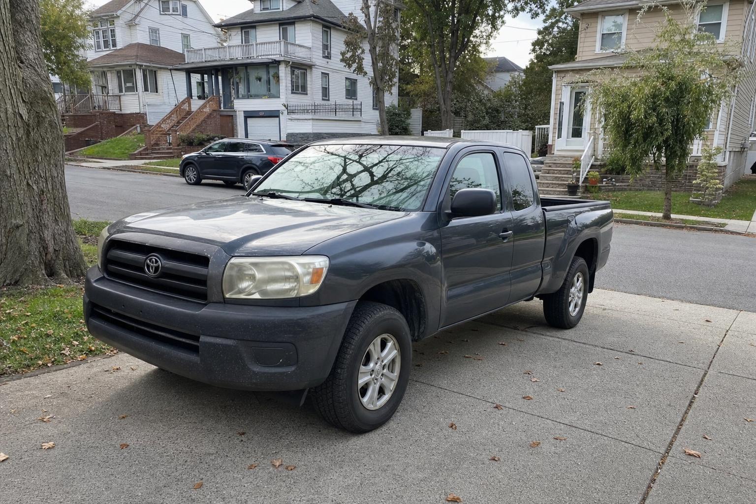 Used pickup truck parked in a Staten Island driveway beside detached homes and mature trees.