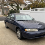 Older sedan parked in a residential Staten Island driveway beneath autumn trees