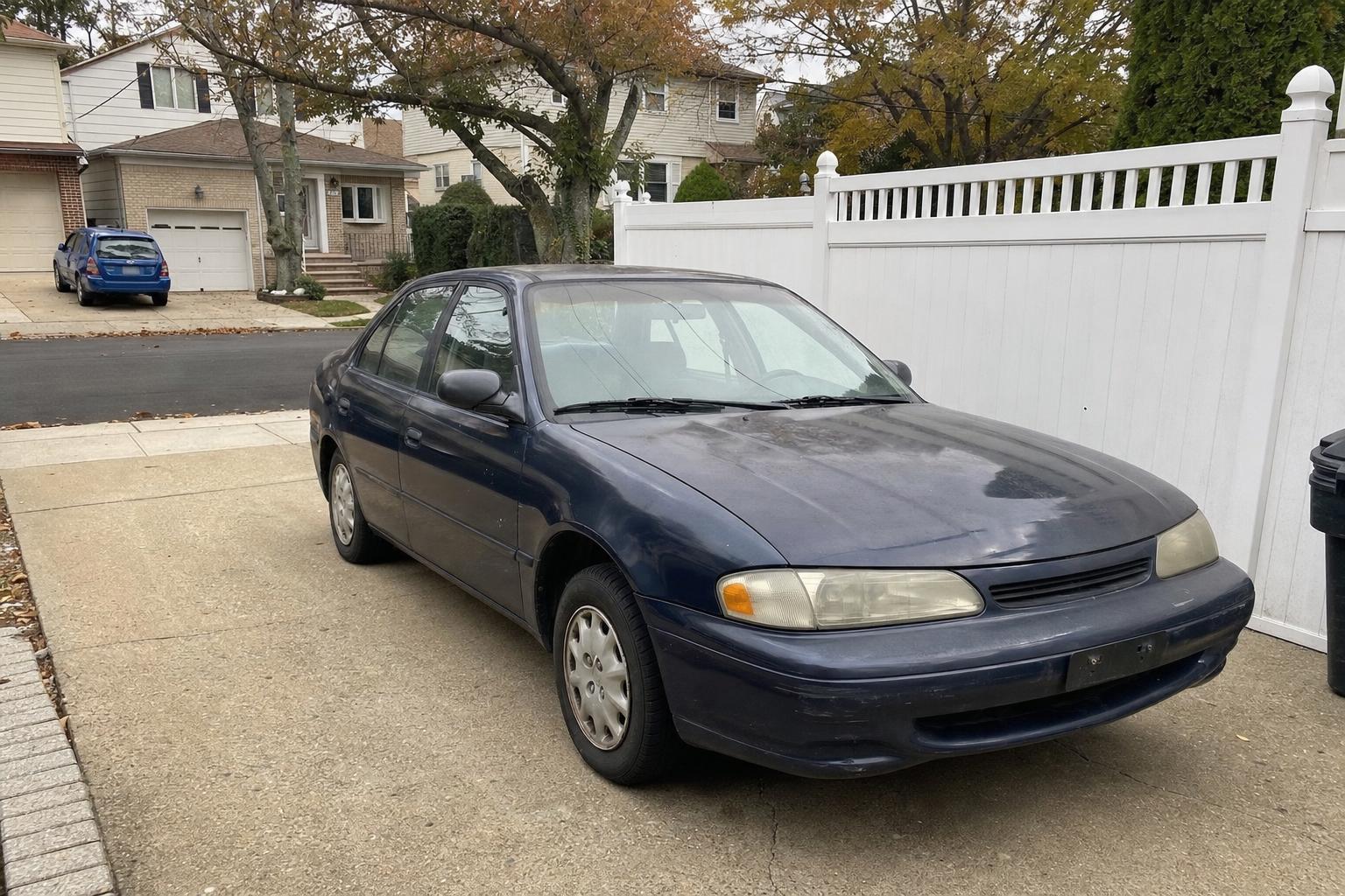 Older sedan parked in a residential Staten Island driveway beneath autumn trees