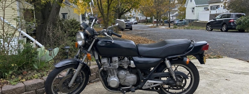 Older motorcycle parked in a Staten Island driveway near detached homes and mature trees.