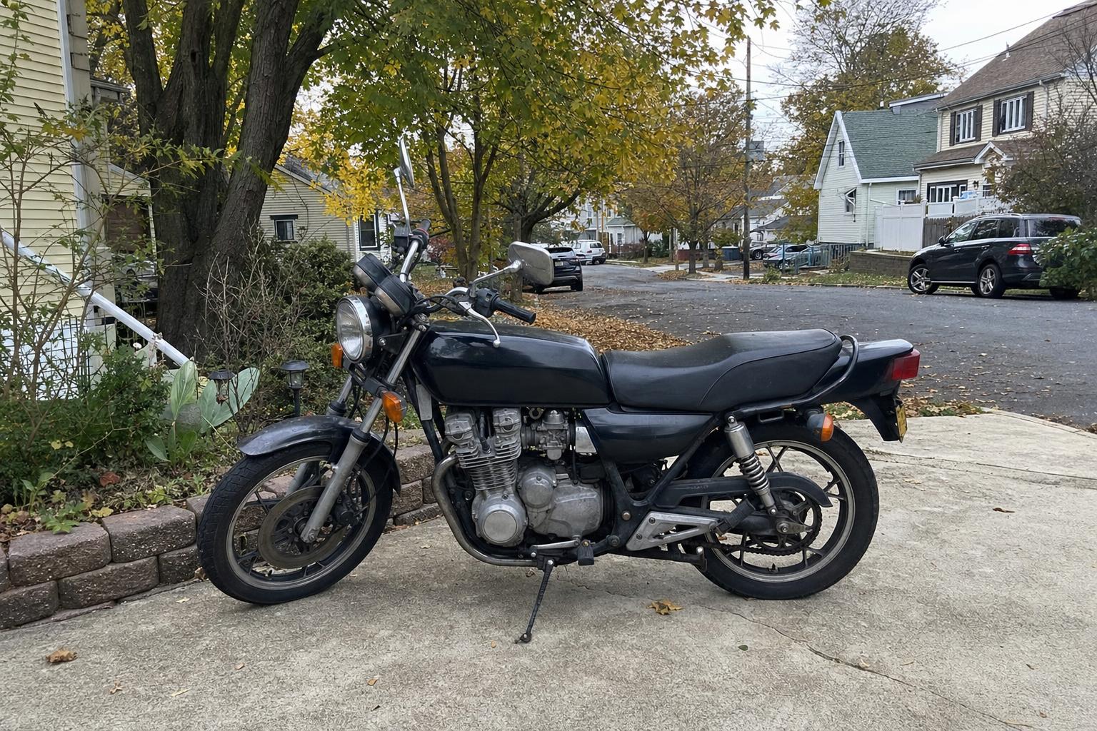 Older motorcycle parked in a Staten Island driveway near detached homes and mature trees.